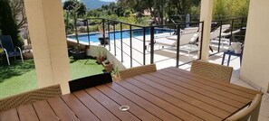 Un tavolo di legno e sedie in vimini su un balcone con vista su una piscina e un'area verde.