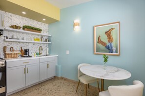 A modern kitchen with white cabinets, a marble countertop, and a dining area with a white table and chairs. - Audrey Suite · Dog yard + pool, 3 min to downtown (Palm Springs)