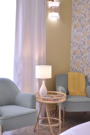 A room with a light blue sofa, a small round table with a white lamp, and a wall with floral wallpaper. - The Audrey Suite · Dog-Friendly Yard & Pool, PS (Palm Springs)