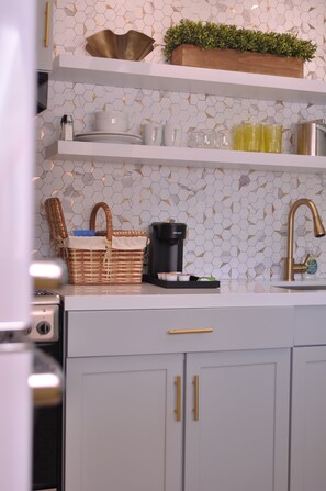 A kitchen with white cabinets, a coffee maker, and a basket on the counter. - The Audrey Suite · Dog-Friendly Yard & Pool, PS (Palm Springs)