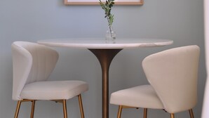 A dining area with a round table, two chairs, and a framed artwork above.