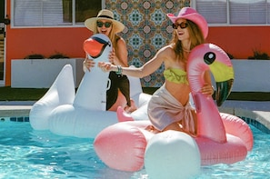 Two people on inflatable flamingos in a swimming pool.