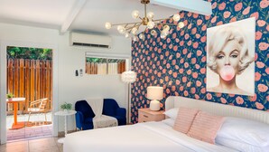 Une chambre à coucher avec un grand lit, une table de chevet, une lampe, une chaise et un mur orné d’un motif floral.