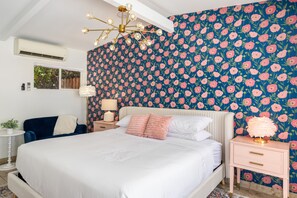 A bedroom with a large bed, a nightstand with a lamp, a chair, and a window with blinds.
