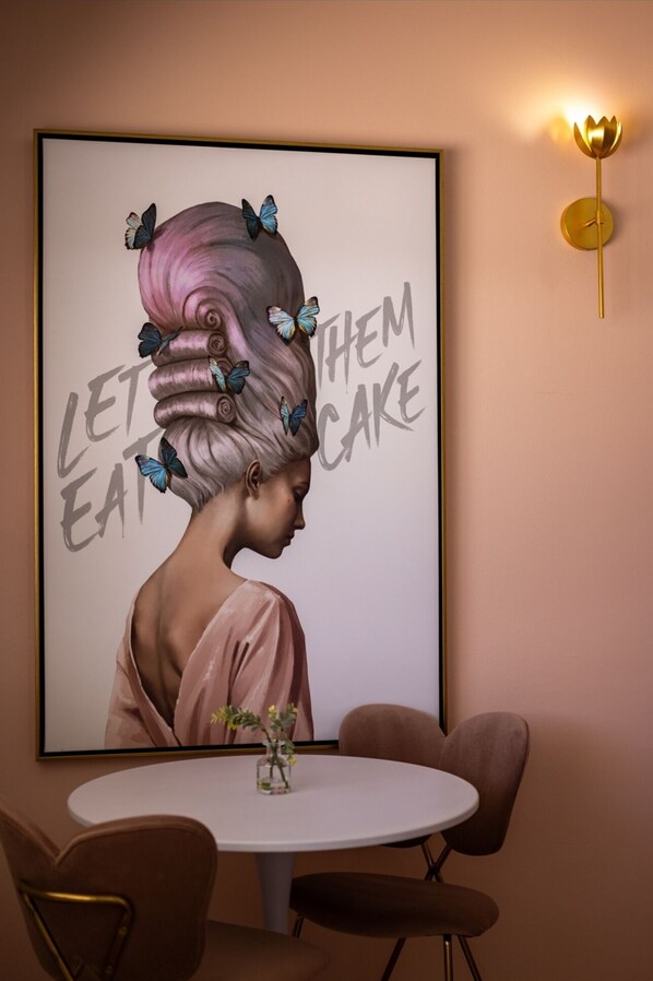 A framed artwork of a woman with butterflies on her hair, with the text "LET THEM EAT CAKE" on a wall.