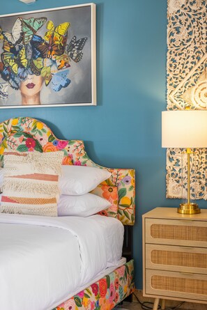 Een slaapkamer met een bloemen hoofdbord, een bedlampje en een wanddecoratie.
