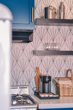 A kitchen with a gas stove, a coffee maker, and a shelf with kitchenware. - The Taylor Suite · Dog-Friendly Yard, Palm Springs (Palm Springs)