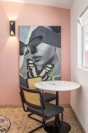 A corner room with a round table, a chair, a wall-mounted light, and a large artwork. - The Taylor Suite · Dog-Friendly Yard, Palm Springs (Palm Springs)