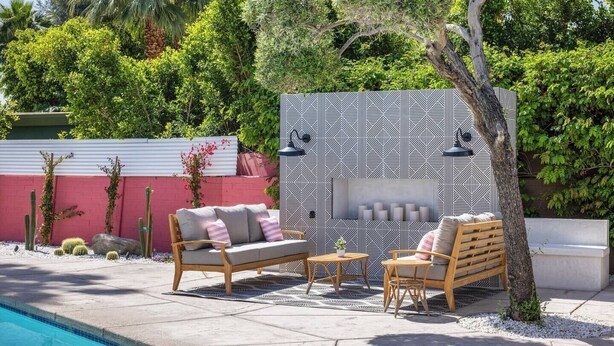 Une terrasse extérieure avec une piscine, un mur décoré de motifs et des espaces aménagés pour s’asseoir.