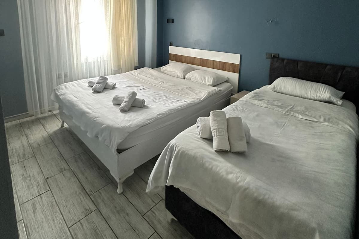 A hotel room with two beds, a wooden floor, and a large window with curtains.