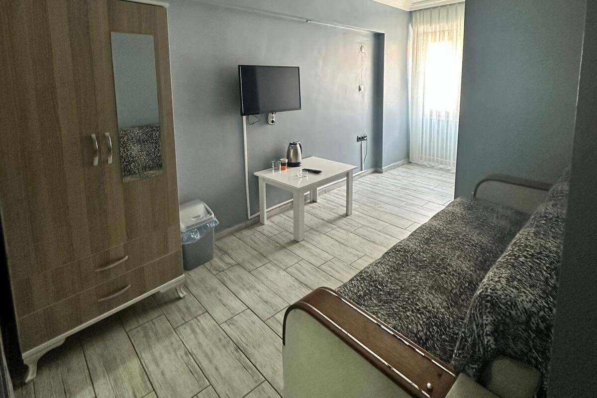 A hotel room with a bed, a TV, a small table, a wardrobe, and a window with curtains.