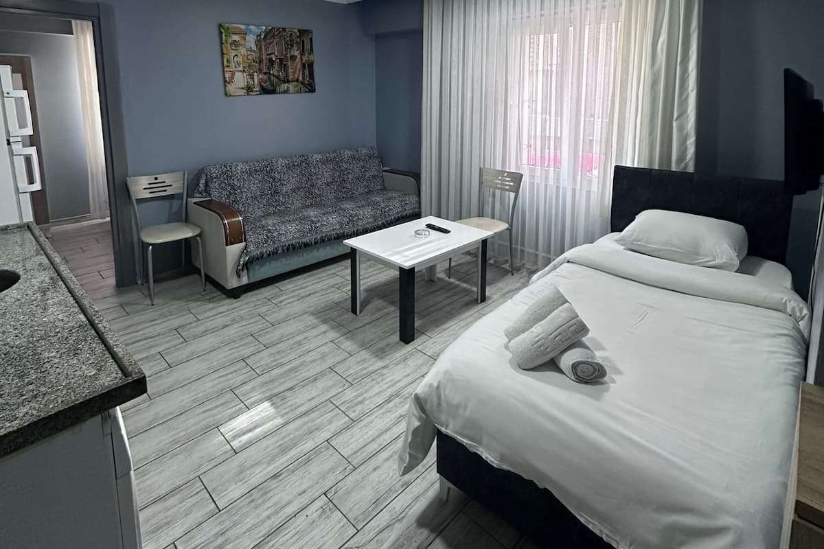 A hotel room with a bed, a sofa, a small table, a chair, and a kitchenette.