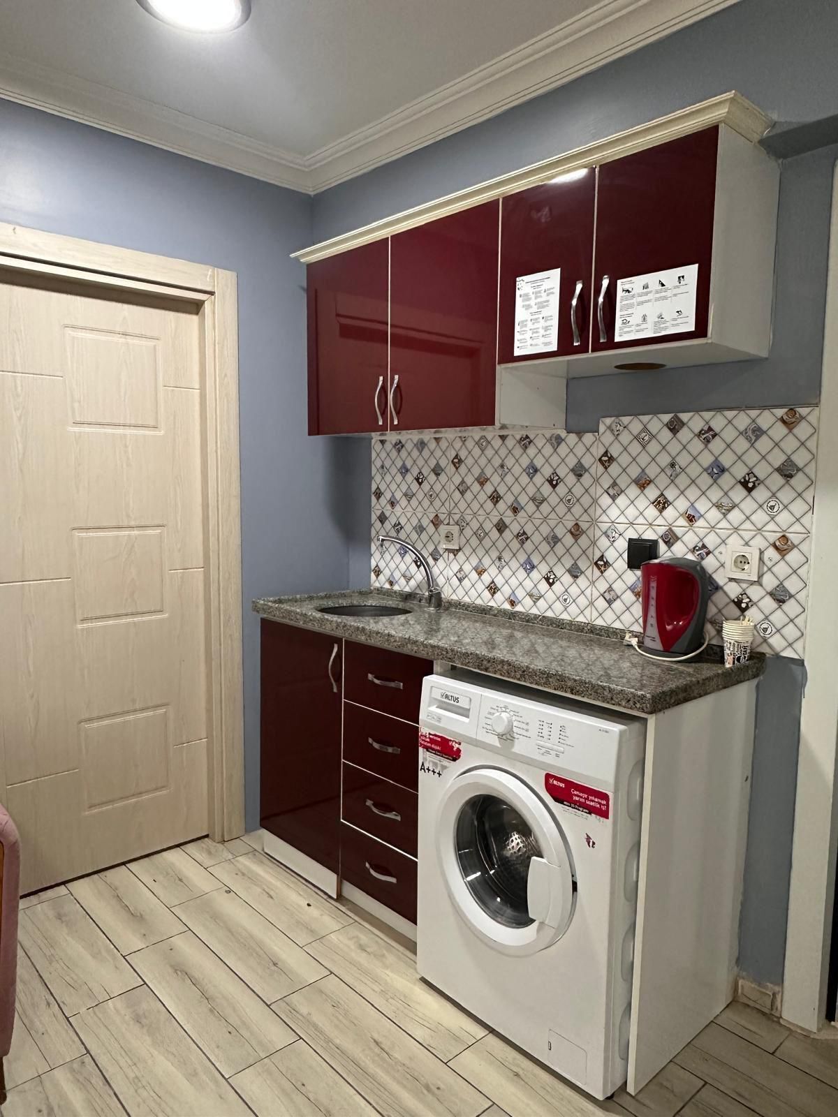 Une cuisine compacte équipée d’un lave-linge, d’un évier et d’un pare-feu en carrelage.