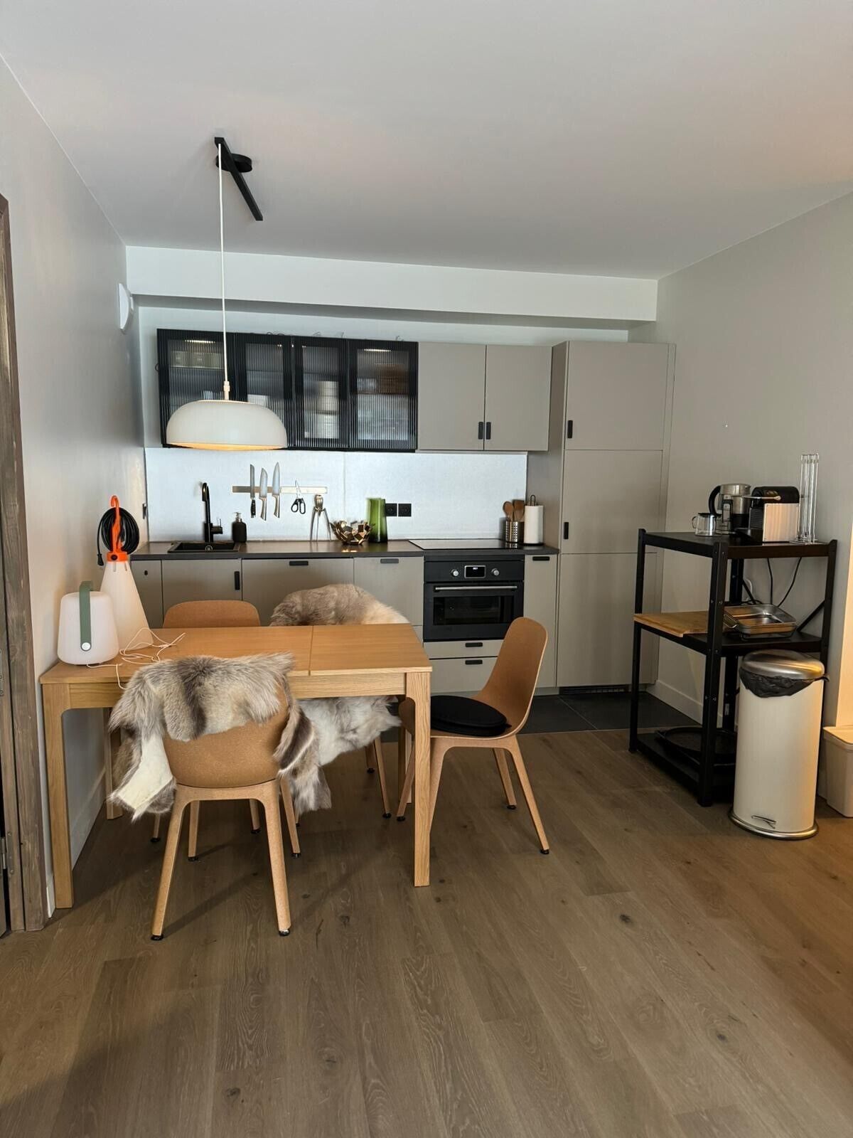 A modern kitchen with a dining area, featuring a wooden table, chairs, and a built-in oven.