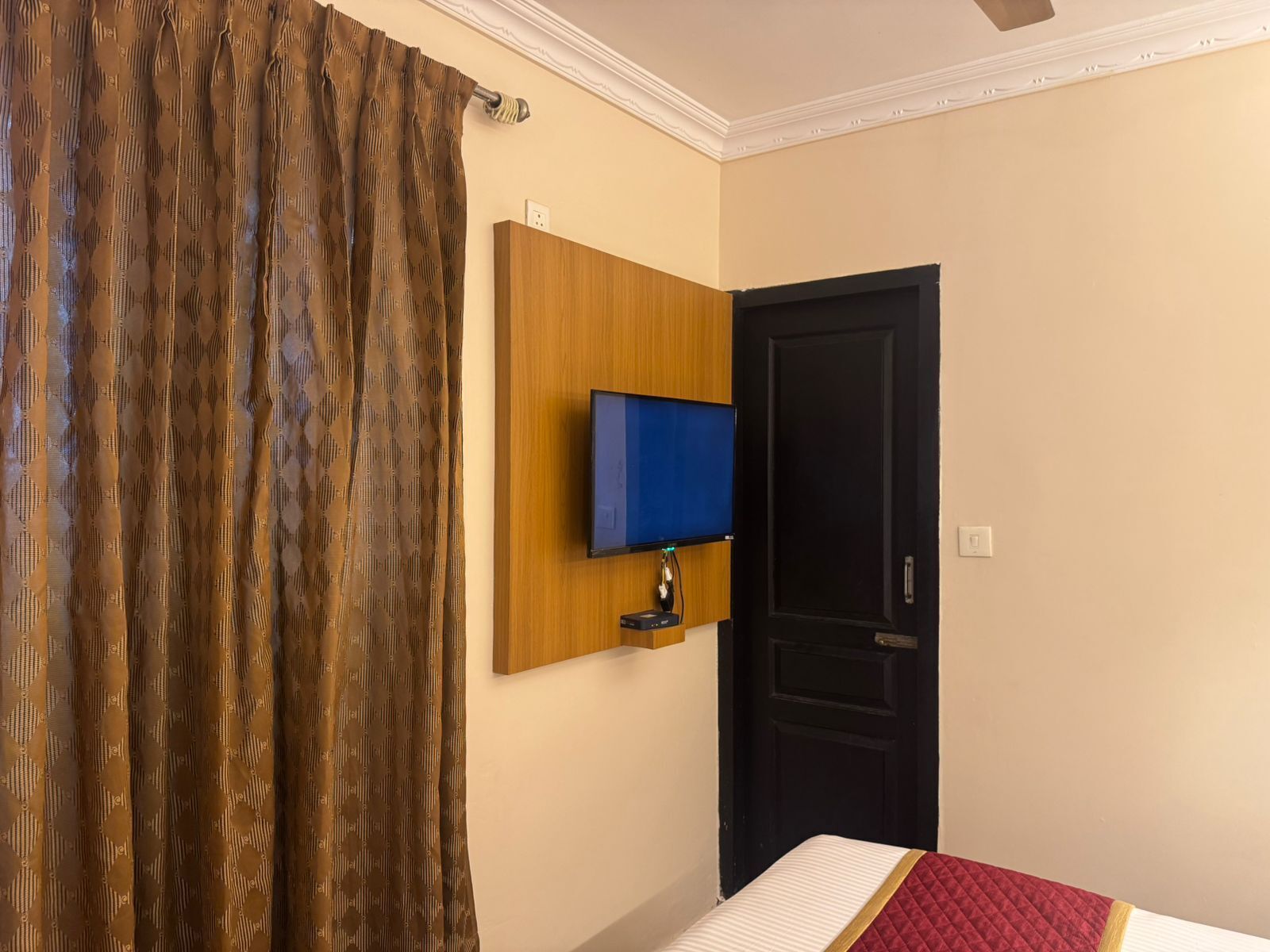 A hotel room with a bed, a television mounted on the wall, a door, and a curtain.
