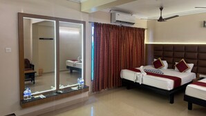 A hotel room with a large mirror, two beds, an air conditioning unit, a ceiling fan, and a reception area with a counter and water bottles. - HOTEL SRIMANIYA (Nagercoil)