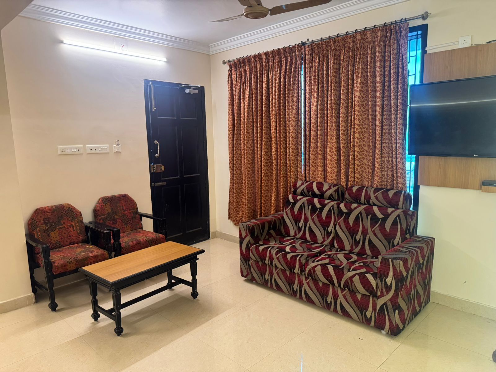 A living room with a sofa, two armchairs, a coffee table, a TV, and a door.