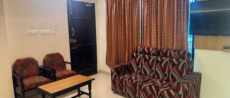 A living room with a sofa, two armchairs, a coffee table, a TV, and a door.