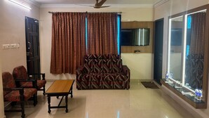 A living room with a sofa, chairs, a coffee table, a TV, and a ceiling fan. - HOTEL SRIMANIYA (Nagercoil)