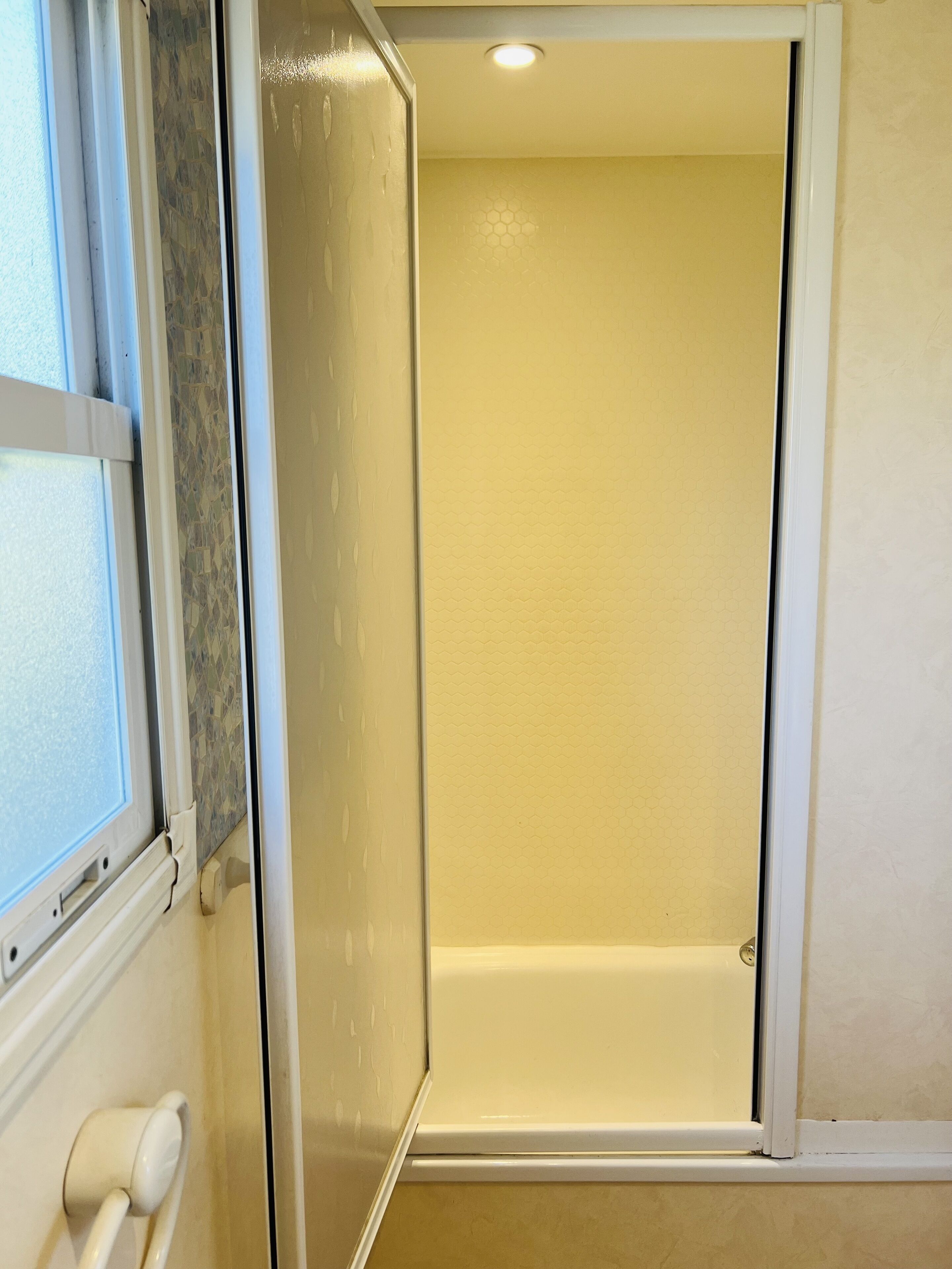 Een badkamer met een douche, toilet en een raam.