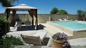 A pool area with a gazebo, lounge chairs, and a small table.