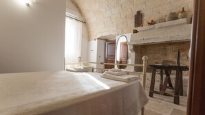 Un dormitorio con una cama grande, una mesita de noche de madera, una chimenea de piedra y un espejo encima.