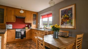 A kitchen with wooden cabinets, a granite countertop, a dining table with chairs, a vase with flowers, and a painting on the wall.