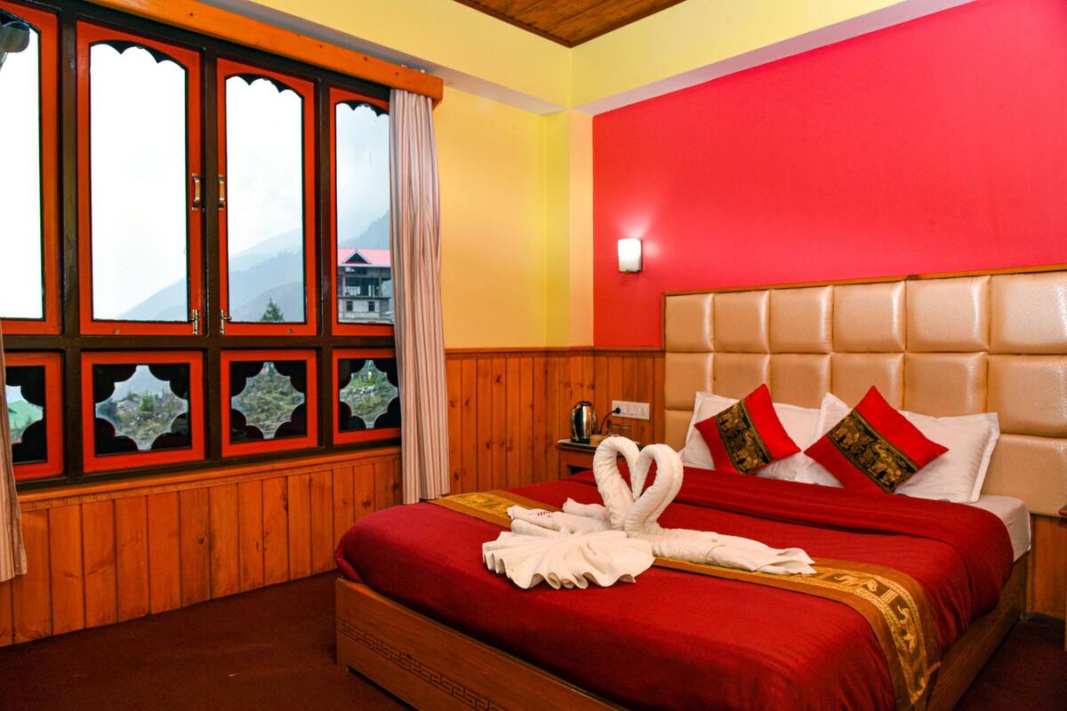 A hotel room with a wooden paneled wall, a red accent wall, and a bed with a red bedspread and white pillows.