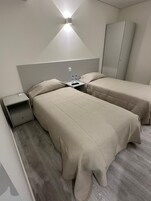 Ein Hotelzimmer mit zwei Betten, einem Kleiderschrank, einem Nachttisch und einer Wandleuchte.