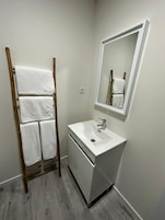 A bathroom with a wooden towel rack holding three towels, a white sink with a mirror above it, and a wooden floor.