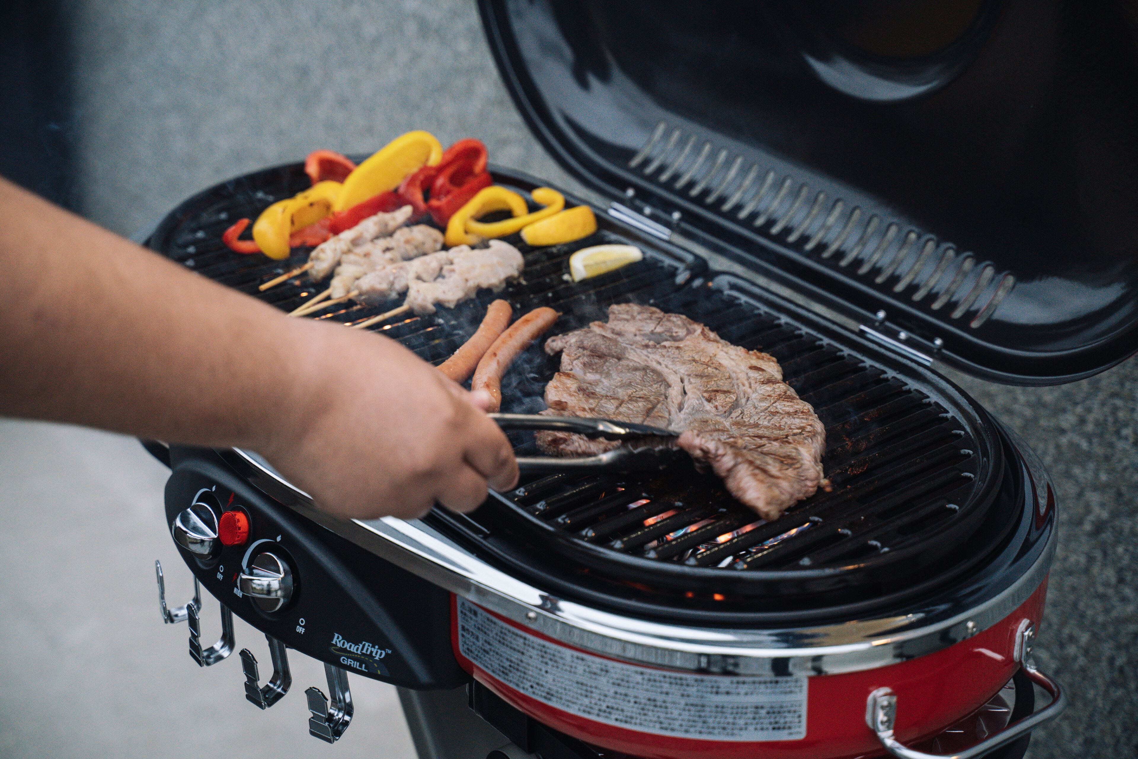 A portable grill with a red exterior and black interior, featuring a handle and control knobs.