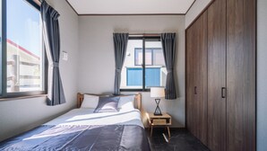 Un dormitorio con cama, mesita de noche, ventana con cortinas, armario y vista a un edificio.
