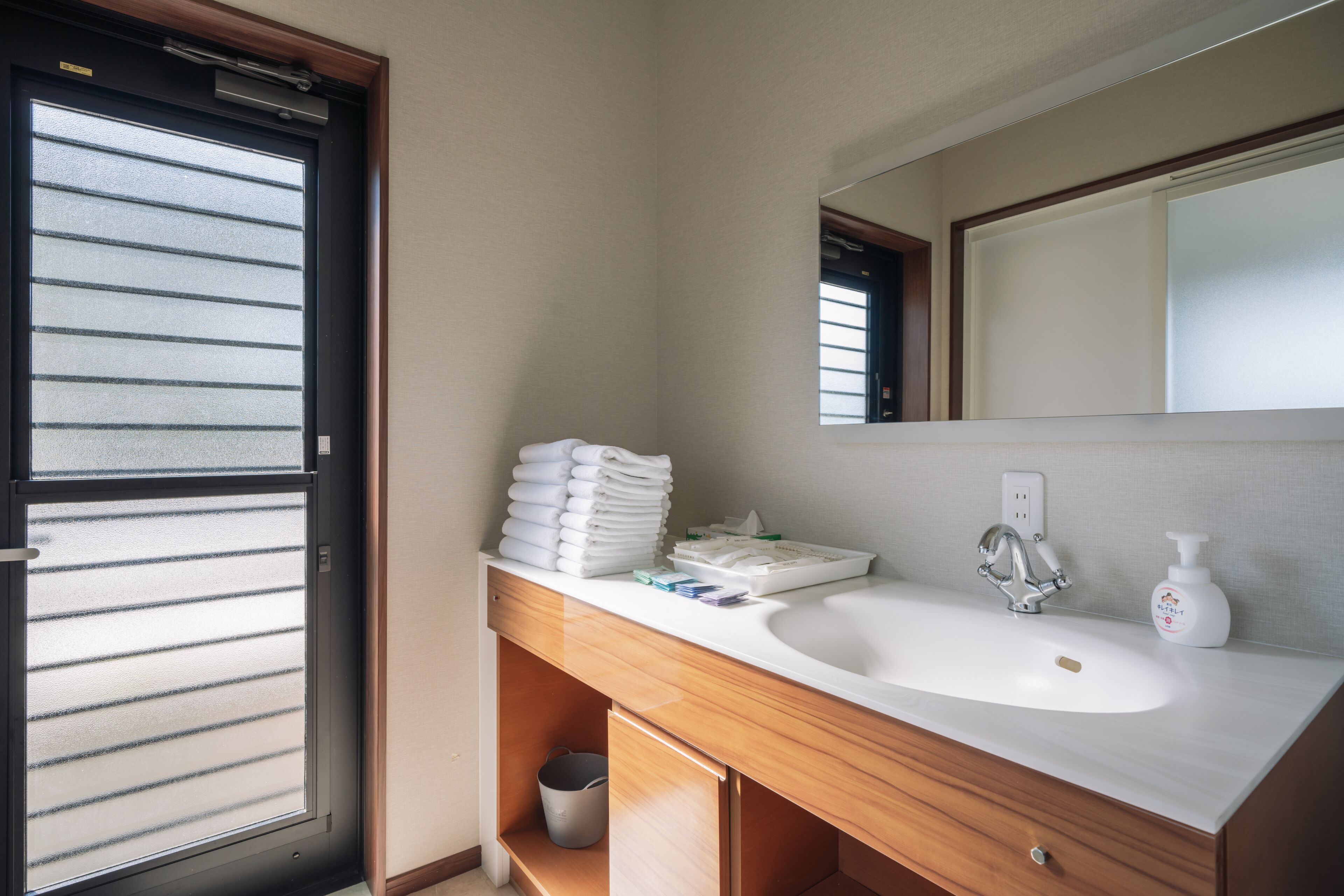 Une salle de bain avec un lavabo blanc, un meuble-lavabo en bois, un miroir et une fenêtre avec des stores.