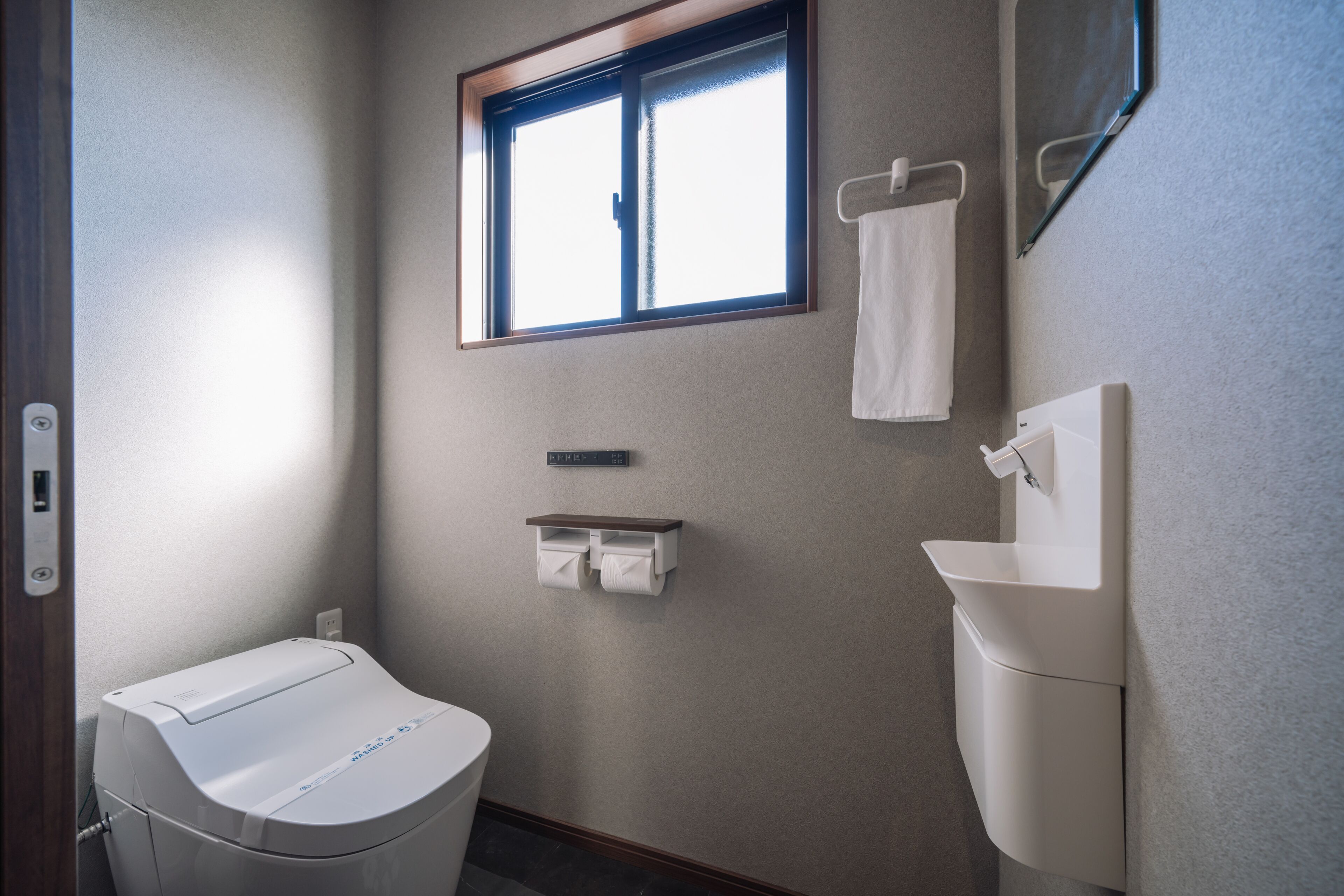 Un baño con inodoro, lavamanos, toallero, ventana y dispensador de toallas.