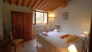 Un dormitorio con una cama grande, un armario de madera, una silla, una ventana con vistas y una lámpara de pared.