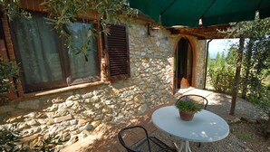 Un edificio de piedra con ventana y persiana, una mesa con una planta en maceta y un espacio exterior cubierto.