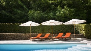 Una piscina con tres sillas reclinables anaranjadas y tres sombrillas.