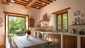 Una cocina con armarios de madera, una mesa de comedor con sillas, un ventanal con vista a zonas verdes y diversos electrodomésticos.