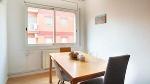 A dining area with a table and chairs, a window with a view of buildings, and a radiator below the window. - Barcelona - Arte (Barcelona)