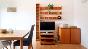 A room with a wooden TV stand, a flat-screen TV, a small cabinet, and a shelf unit with plants. - Barcelona - Arte (Barcelona)