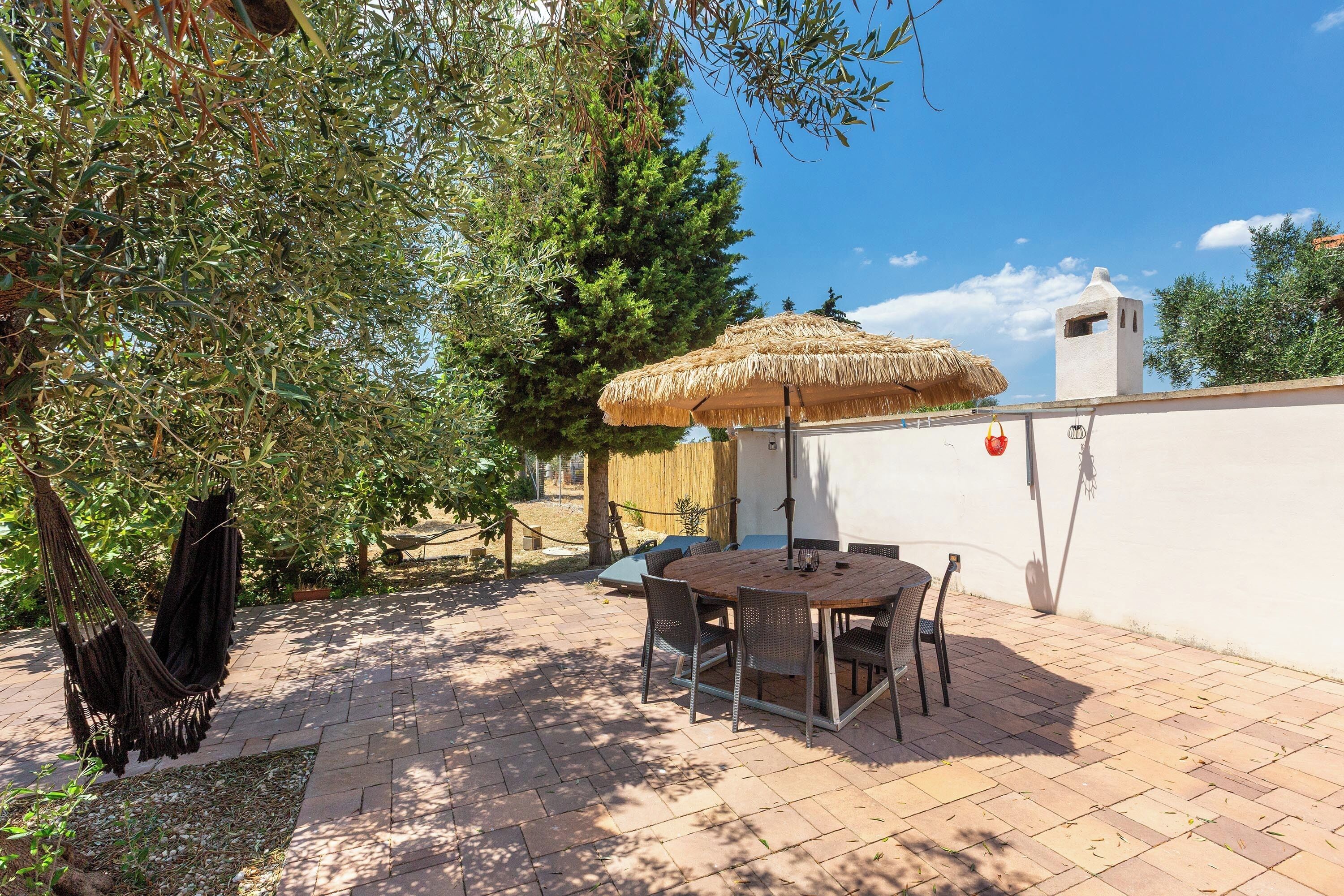 An outdoor patio with a table and chairs, a thatched umbrella, and a white wall.