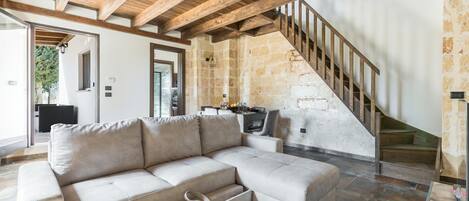 A modern living room with a sectional sofa, a wooden staircase, and a stone wall.