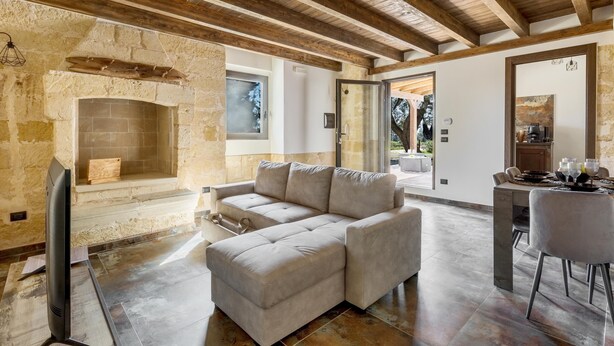 A modern living room with a stone fireplace, a sectional sofa, and a dining area with a table and chairs. - 3775 Villetta Mora by Barbarhouse (Nardò)