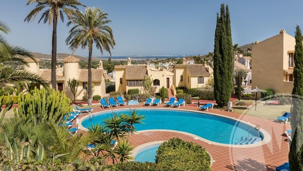 A resort with a swimming pool surrounded by palm trees and lounge chairs. - La Manga Club El Rancho Townhouse 513 (Atamaría)