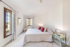 A bedroom with a large bed, a nightstand, a chair, and a window with curtains. - La Manga Club El Rancho Townhouse 513 (Atamaría)