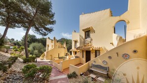A courtyard with yellow buildings, a stone pathway, and a bench. - La Manga Club El Rancho Townhouse 513 (Atamaría)
