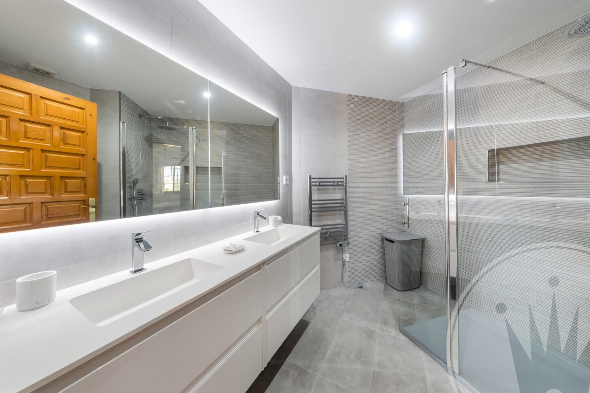 A modern bathroom with a large mirror, two sinks, a shower, and a glass-enclosed shower area.