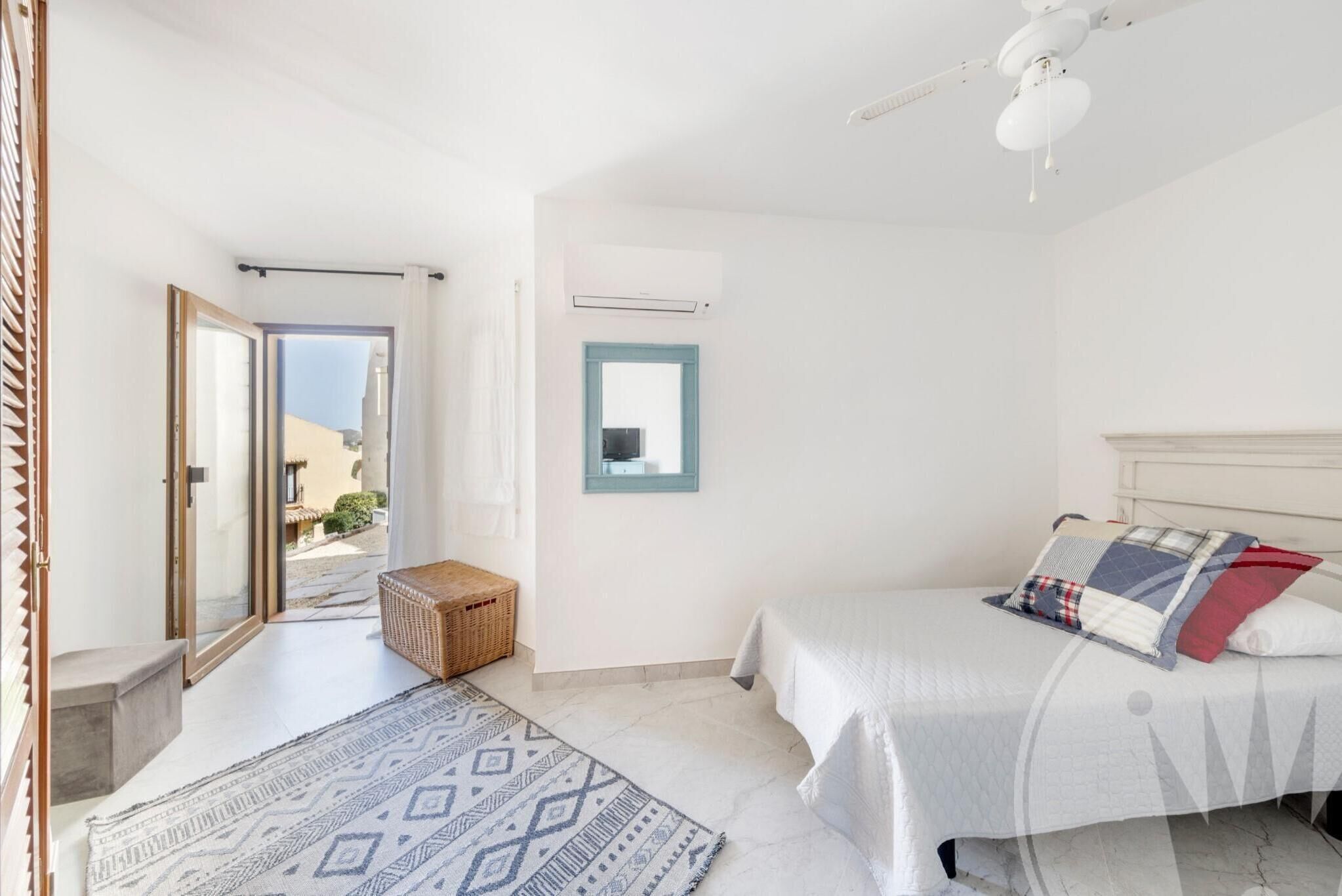 Une chambre à coucher avec un lit, un ventilateur de plafond, une fenêtre donnant sur un beau paysage et une porte menant à l’extérieur.