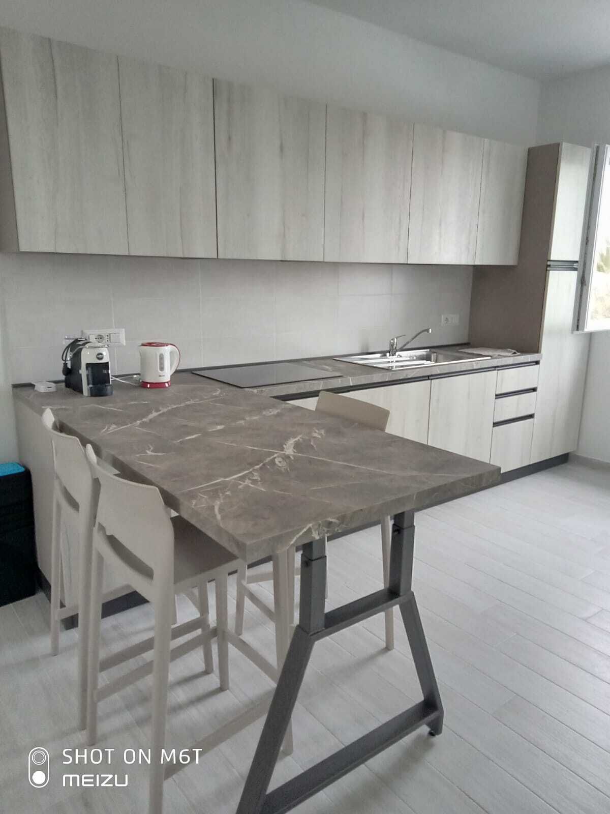 A modern kitchen with a marble countertop, white cabinets, and a coffee maker.