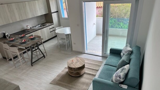 Un saló modern amb un sofà, una taula de dinar amb cadires, una zona de cuina i una porta corredissa de vidre que dona a un balcó.